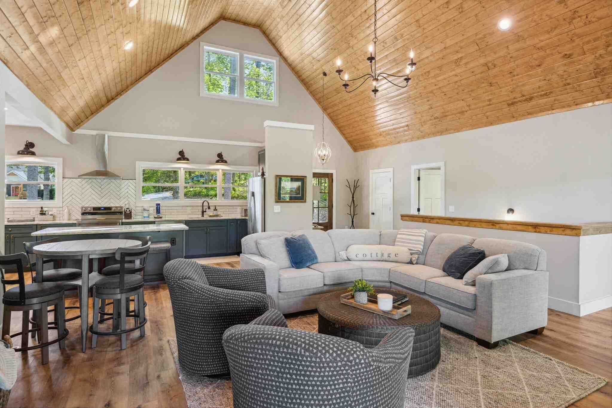 A spacious living area with a high ceiling, a grey sectional sofa, a round coffee table, and a dining set.