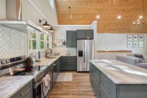 A modern kitchen with a herringbone tile backsplash, stainless steel appliances, and a wooden ceiling. - Mcdonald Lakeside Cottage (Sevierville)