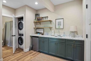 A laundry room with a washing machine, shelves with glassware, a sink, and cabinets. - Mcdonald Lakeside Cottage (Sevierville)