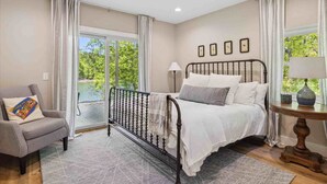 A bedroom with a bed, a chair, a table, and a view of greenery outside. - Mcdonald Lakeside Cottage (Sevierville)