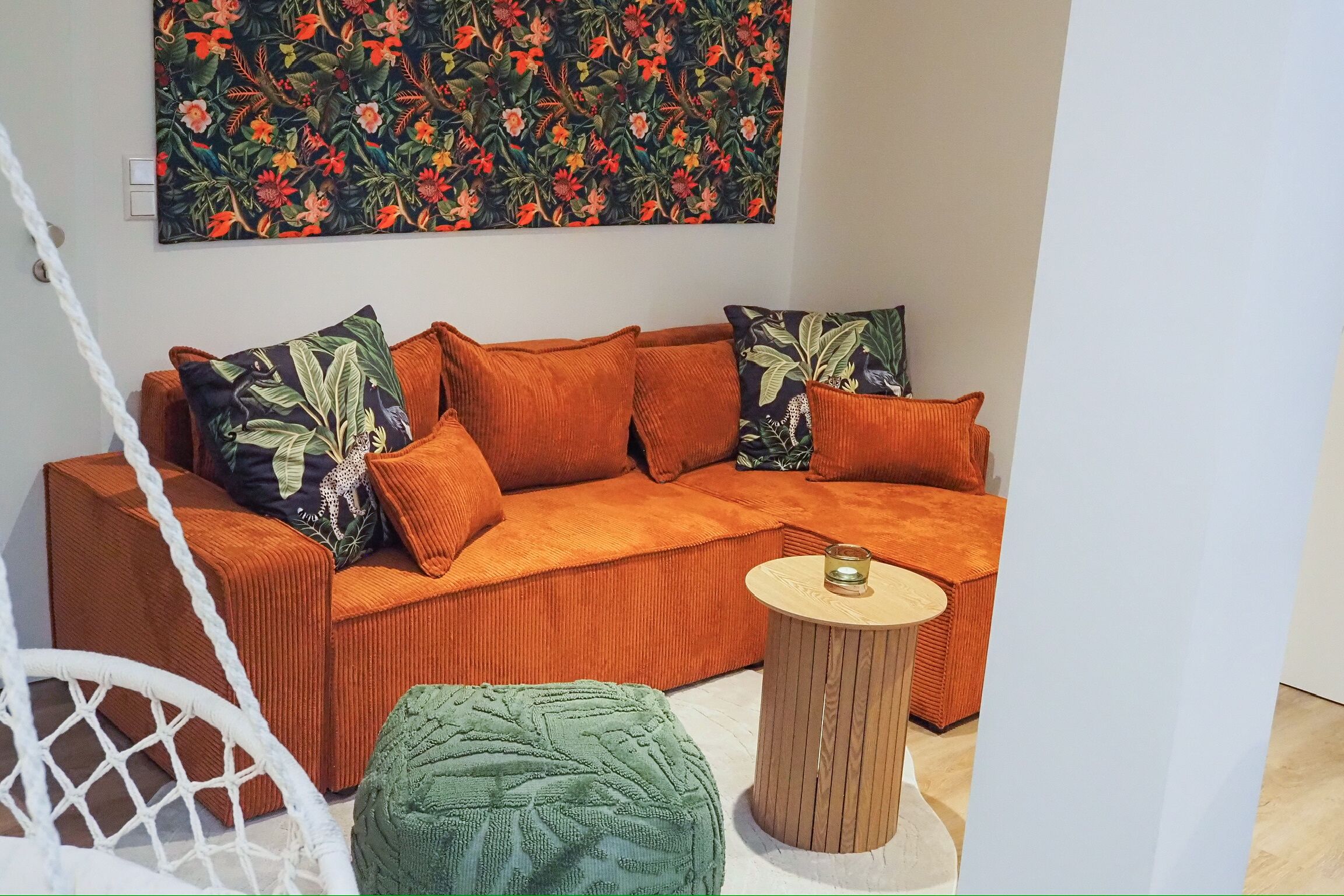 A modern living room with a sofa, green ottoman, and a small wooden side table.