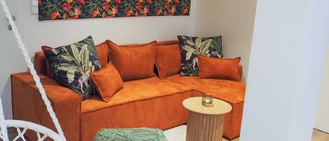 A modern living room with a sofa, green ottoman, and a small wooden side table.
