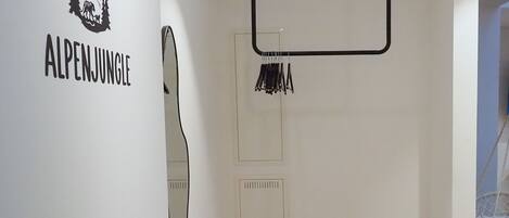 A room with a metal rack, a hanging coat rack, and a door with a mirror.