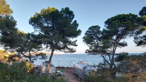 A seaside setting with a trailer and a boat, surrounded by trees and a clear view of the sea. - Camping Laplaya Ibiza (Santa Eulalia del Rio)