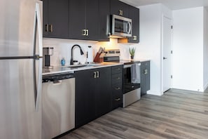 A modern kitchen with dark cabinetry, stainless steel appliances, and a wooden floor. - Landing Apartments Downtown Salt Lake City Near Trolley Square (Salt Lake City)