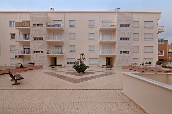 A multi-story residential building with balconies, a central courtyard with benches, and potted plants.