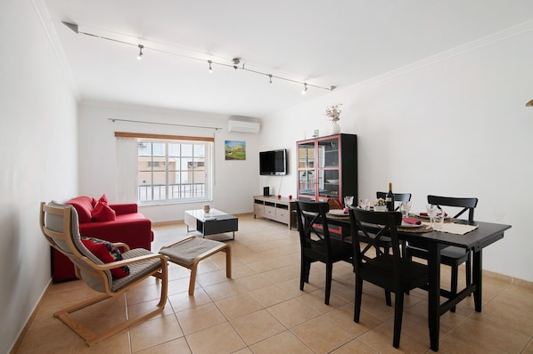 Un salon comprenant un canapé, une table à manger avec des chaises, un téléviseur et un meuble.