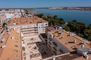 A coastal urban area with terracotta-roofed buildings, a marina, and a clear blue sea.