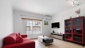 A modern living room with a red sofa, a coffee table, a TV, and a cabinet with glass doors. - Apartment 'Guadiana' with Balcony, Wi-Fi and Air Conditioning (Vila Real de Santo António)