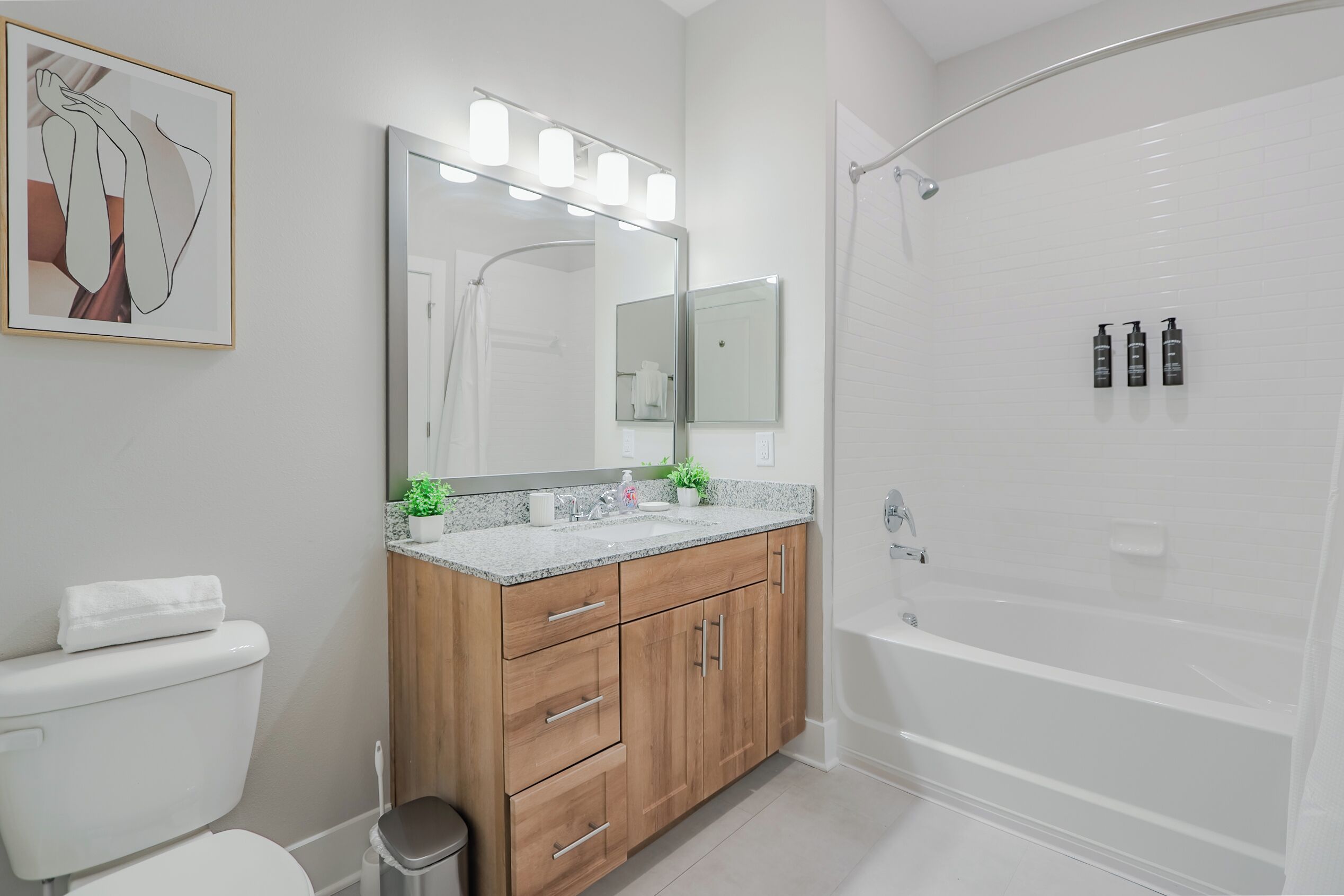 Un baño moderno con tocador de madera, un espejo grande con iluminación, un inodoro blanco y una bañera.