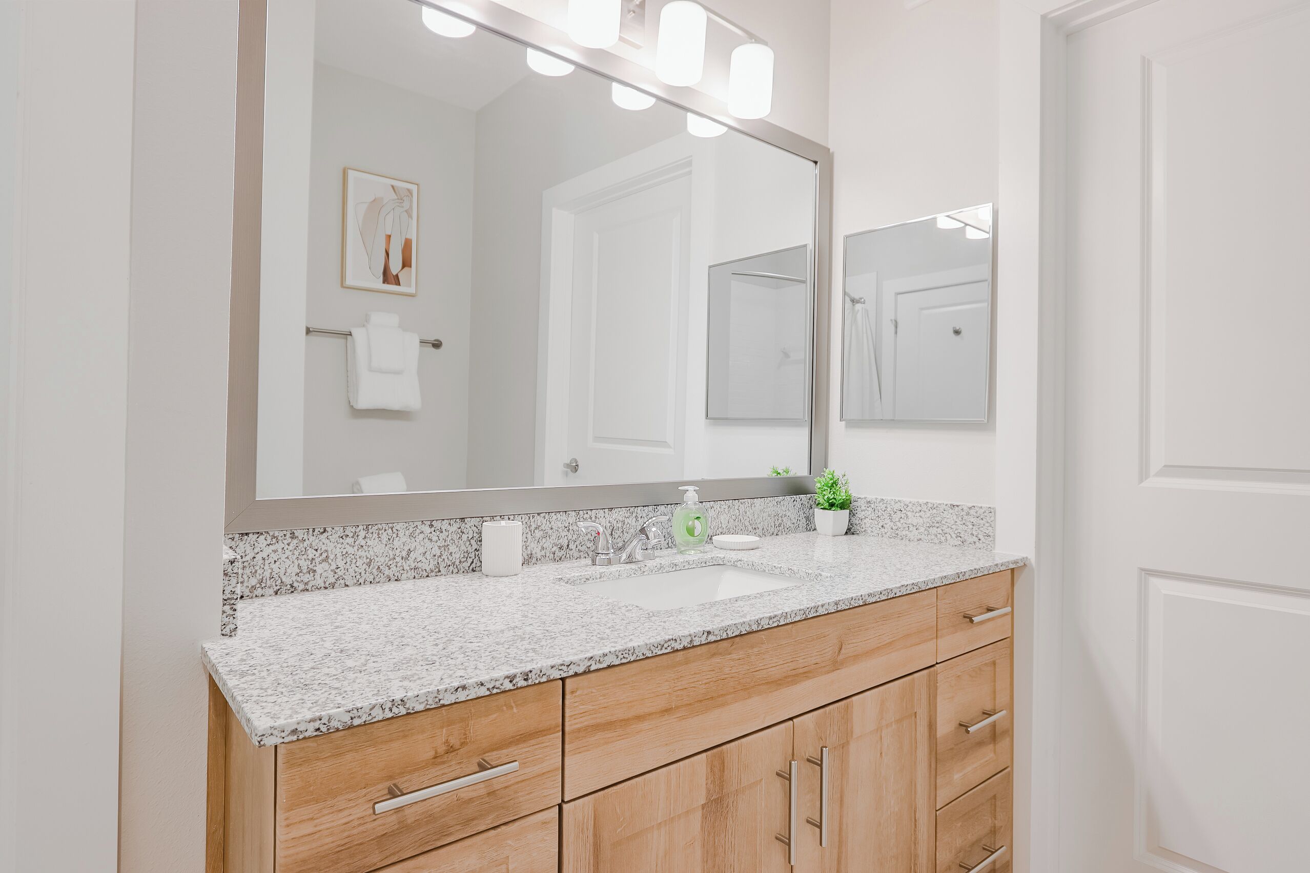 A bathroom with a granite countertop, a sink, a mirror, and wooden cabinets.