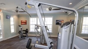 Et fitnesscenter med forskellige træningsmaskiner, en bænk og et tvophængt fjernsyn.