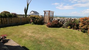 A backyard with a lawn, a wooden fence, a stone wall, and a wooden pergola. - Goetra (Harlech)