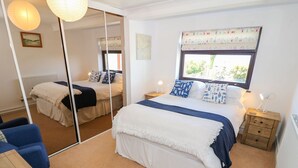 A bedroom with a large bed, a mirror, a window with curtains, a bedside table with a lamp, and a chair. - Goetra (Harlech)