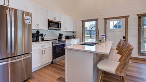 A modern kitchen with white cabinetry, stainless steel appliances, and a central island with bar stools. - Little Haven Chalet (Pigeon Forge)