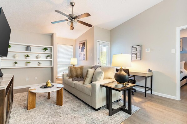 A living room with a ceiling fan, a sofa, a coffee table, a TV, and a lamp. - Landing Apartments Near AT&T Stadium & Six Flags (Arlington)