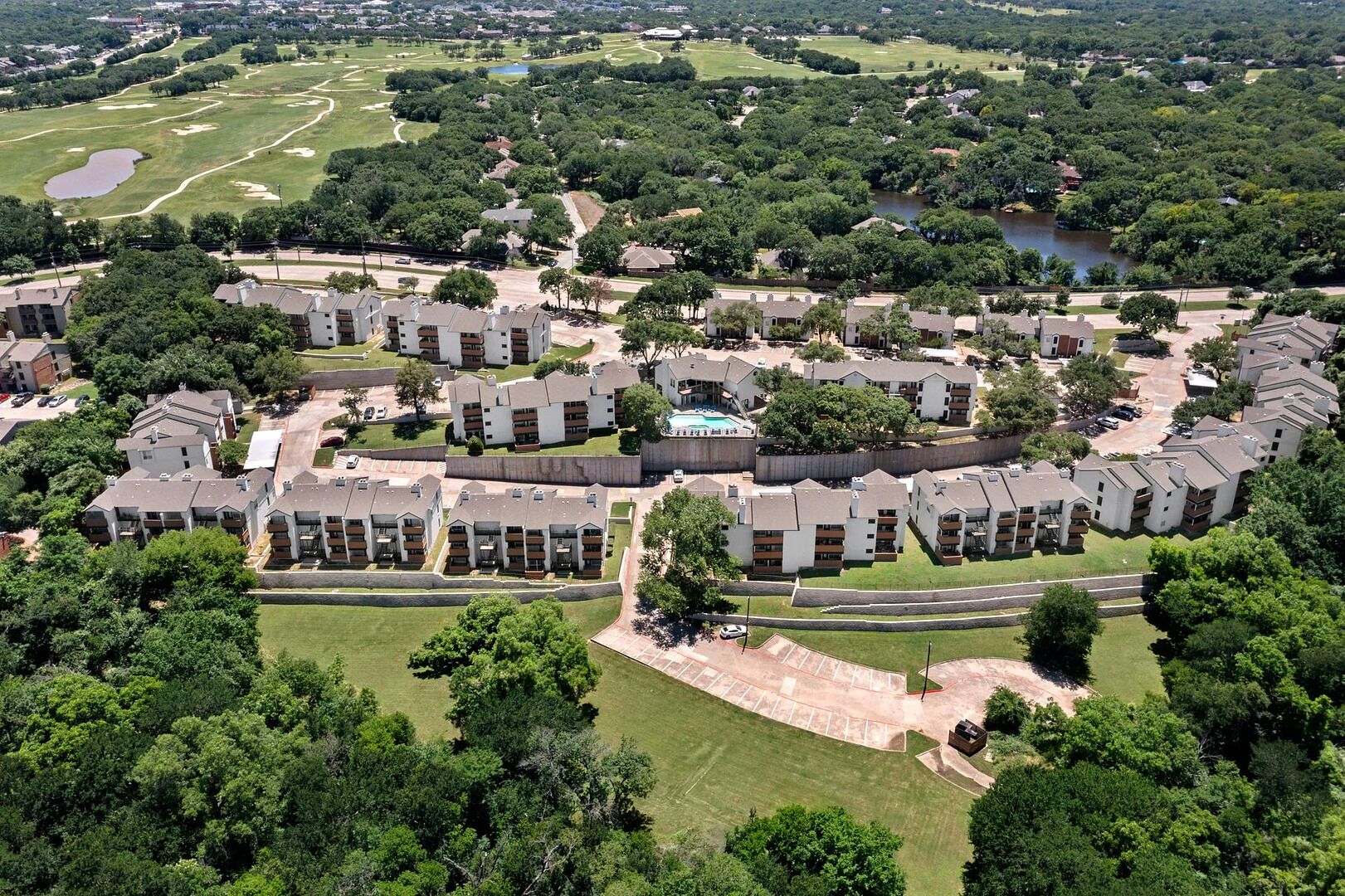 An aerial view of a residential complex with multiple apartment buildings, green lawns, and a golf course in the background.
