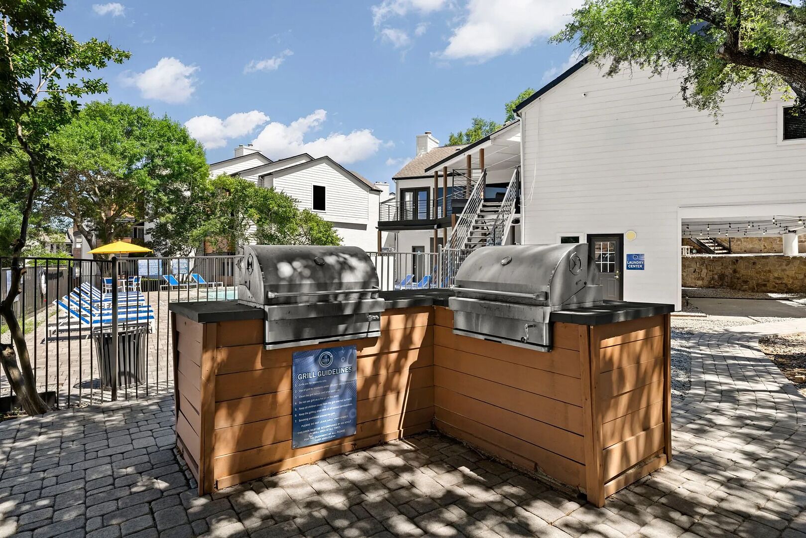 An outdoor grill area with a sign detailing grill guidelines, a covered seating area, and a laundry center nearby.