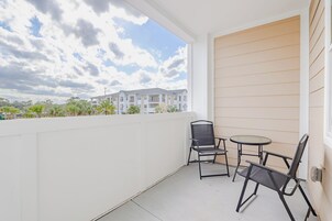 Un balcón con dos sillas y una mesita, con vistas a una zona residencial con edificios y vegetación.