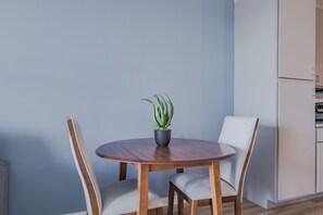 Ein runder Holztisch mit zwei Stühlen, einem Blumentopf und einer Küchenzeile mit Schränken.
