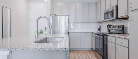 Una cocina moderna con armarios blancos, un refrigerador de acero inoxidable, un microondas y una estufa.