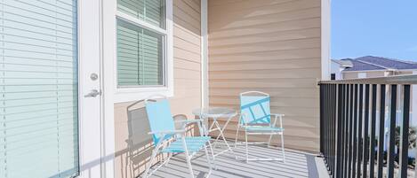 Een balkon met twee blauwe stoelen en een kleine tafel, beigekleurige wanden en een uitzicht op omliggende huizen.