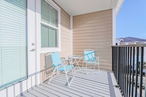 Ein Balkon mit zwei blauen Stühlen und einem kleinen Tisch, helbeige Wände und Blick auf angrenzende Häuser.