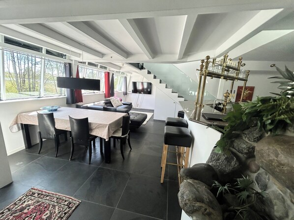 A modern interior with a dining area, a sofa, a staircase, and a kitchen area.