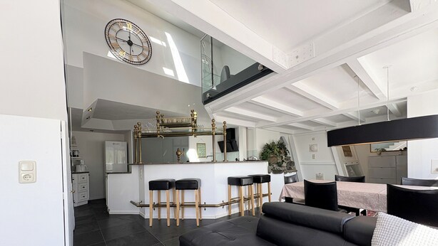Ein modernes Wohnzimmer mit einer schwarzen Ledersofa, einem Essbereich mit Tisch und Stühlen sowie einer Küche mit Bar.