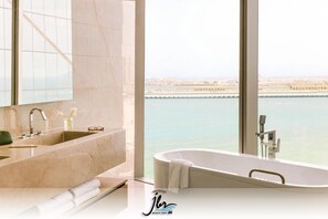 A modern bathroom with a large bathtub and a dual sink, featuring a city view through large windows. - Premium Iconic Beachside JBR Stay (Dubai)