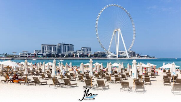 A beach with numerous sun loungers and umbrellas, a large Ferris wheel, and a cityscape in the background. - Premium Iconic Beachside JBR Stay (Dubai)