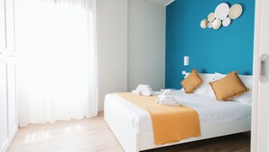 A hotel room with a bed, white curtains, a blue accent wall, and a wooden floor. - [Bari Oberdan Home & Charm 1] Central Apartment (Bari)