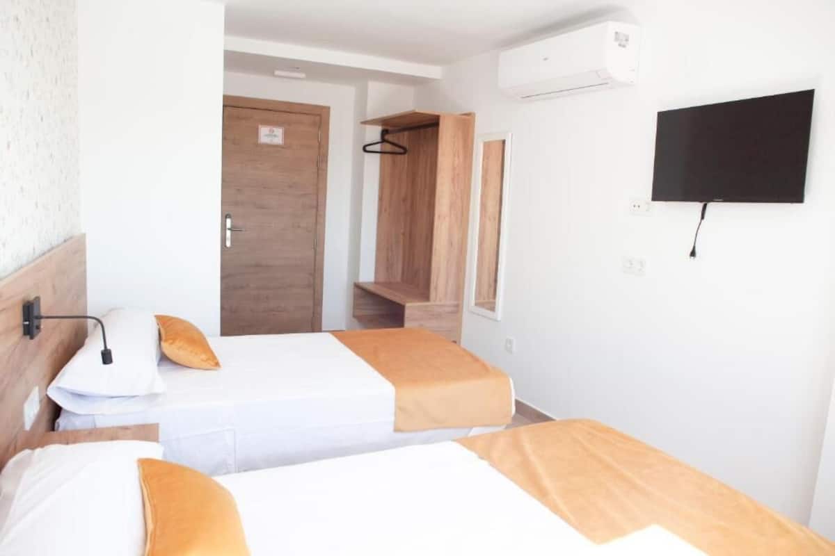 Habitación de hotel con dos camas, un armario de madera, un televisor montado en la pared y una puerta que da a un baño.