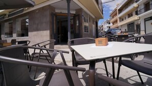 Ein Café mit Außenbereich, Tischen, Stühlen und einem Hauseingang, bewölkter Himmel.