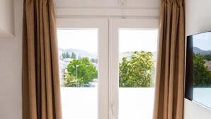Ein modernes Zimmer mit einer Schiebetür aus Glas, einem weißen Stuhl, einem kleinen runden Tisch mit einer Lampe und einem an der Wand montierten Fernseher.