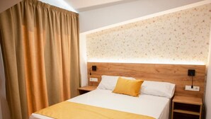 Ein ordentlich bezogenes Bett mit weißer und gelber Bettdecke, einem Holz-Kopfteil und zwei Nachttischen mit Lampen.