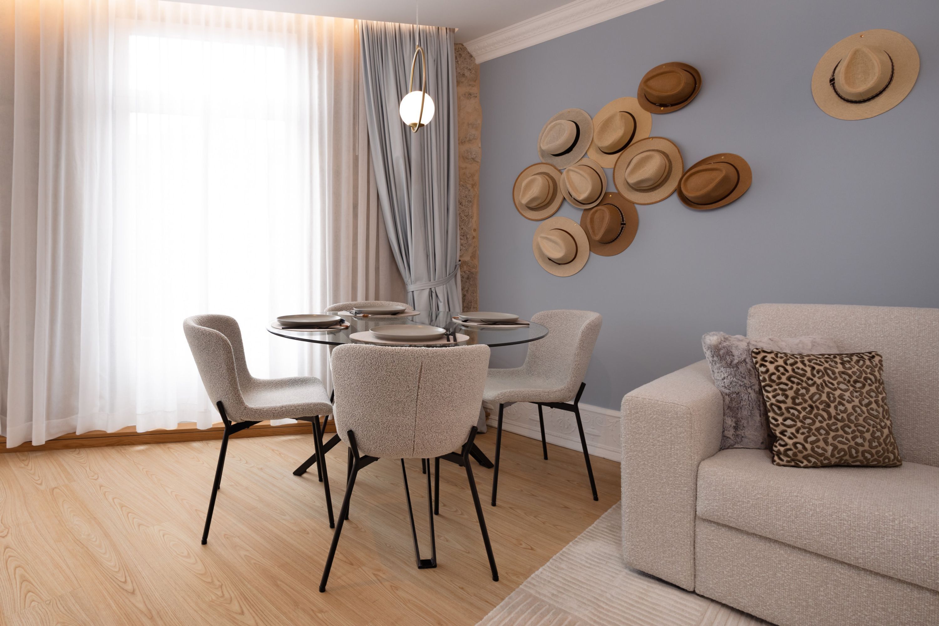 Un comedor con una mesa redonda y sillas, un sofá, y una pared con sombreros.
