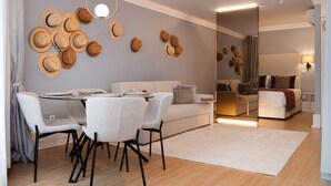 Un salon moderne avec un coin repas, comprenant un canapé, des fauteuils, une table basse et un mur décoré de chapeaux.
