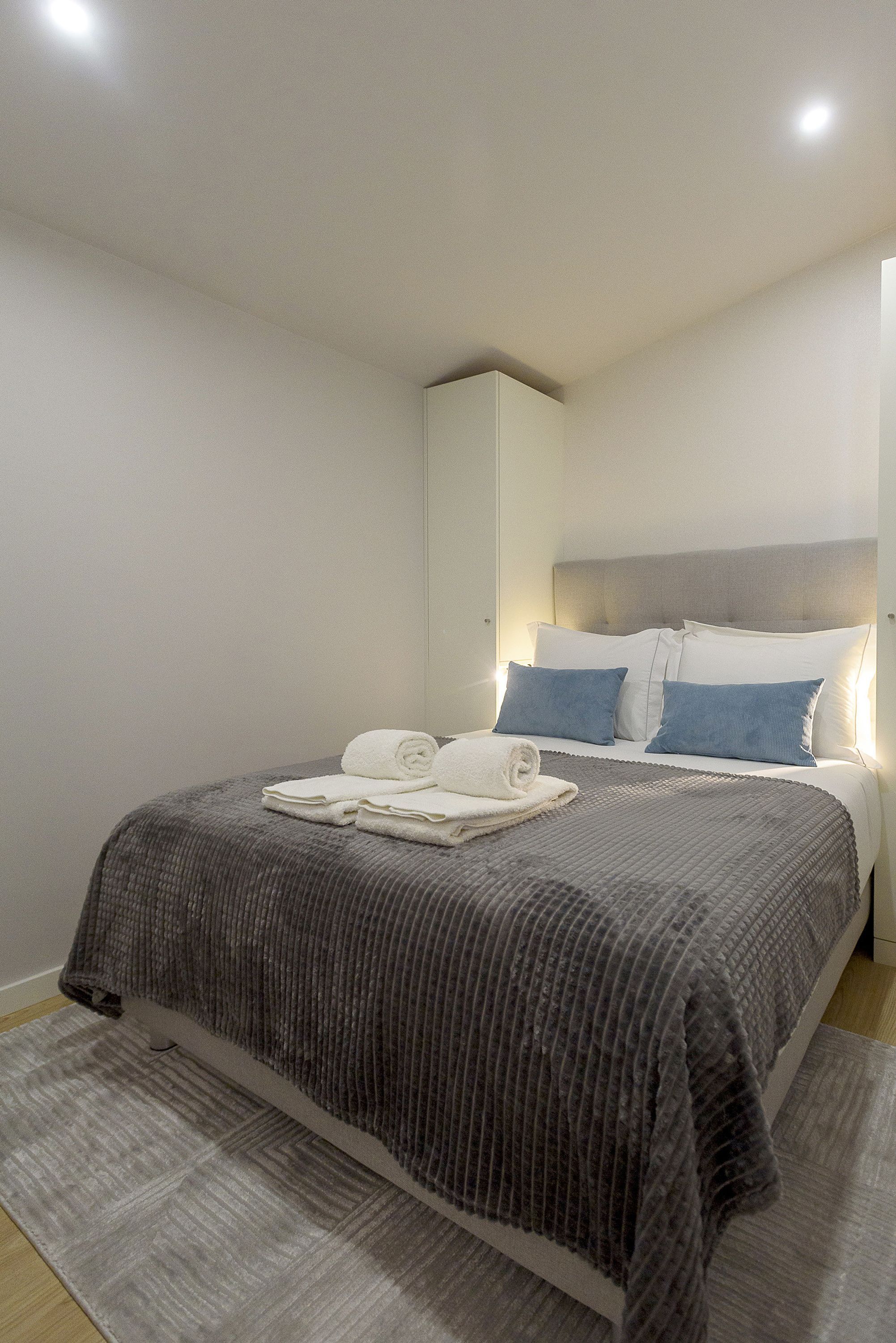 A neatly made bed with a grey and white striped bedspread, two pillows, and a folded towel on the bed.