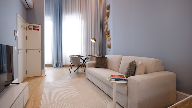Un salon moderne comprenant un canapé, une petite table avec des livres, un coin repas avec des chaises et un buffet.
