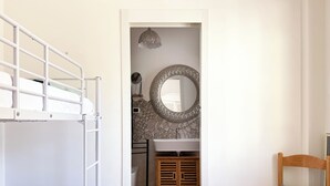 A bedroom with a bunk bed, a wooden chair, and a bathroom with a sink and mirror.