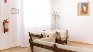 A room with two wooden beds, a white curtain, a fire extinguisher, a floor lamp, and a framed picture on the wall.