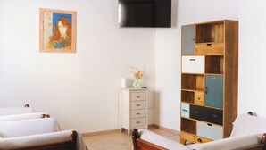 A room with two beds, a TV, a painting, and a wooden cabinet with multiple compartments.