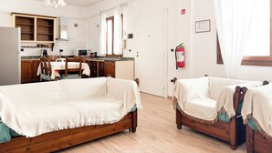 A cozy room with a wooden bed, a dining table with chairs, a kitchen area with cabinets and a microwave, and a window with curtains.