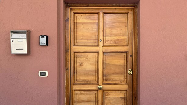 A wooden double door with a brass handle, a mail slot, and a keypad on the wall beside it.