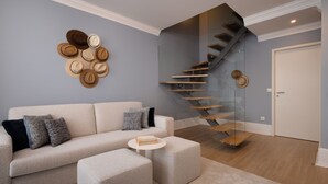 A modern living room with a sofa, ottoman, and a coffee table. A staircase with wooden steps and glass railings leads to an upper level. - RA - Flores 4 in Oporto (Porto)