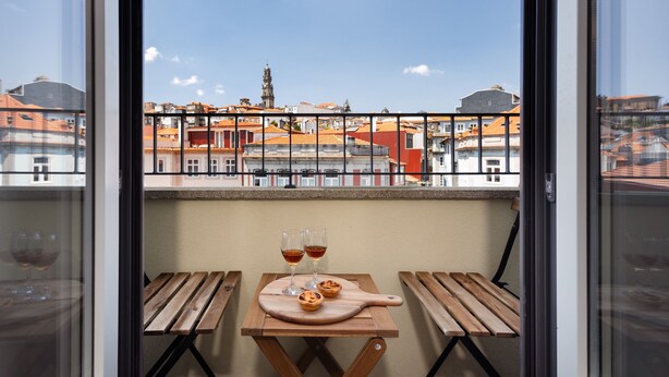 A balcony with a wooden table, two glasses of wine, and a small pastry on a wooden board. - RA - Flores 4 in Oporto (Porto)