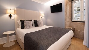 A modern bedroom with a large bed, two bedside lamps, a flat-screen TV, and a stone wall. - RA - Flores 4 in Oporto (Porto)