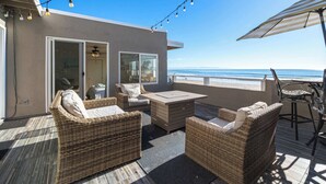 A deck with wicker furniture, a table, and an umbrella. - Beachfront Aptos Home - Right on the Sand! (Aptos)
