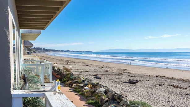 A beach view from a balcony with a railing, a pathway, and a rocky shoreline. - Beachfront Aptos Home - Right on the Sand! (Aptos)